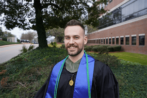Chris Foley, BS in Healthcare Studies 2019 standing outside in his regalia. 