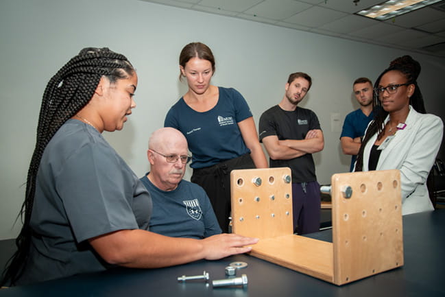 OT faculty observe while students work with patient hand function