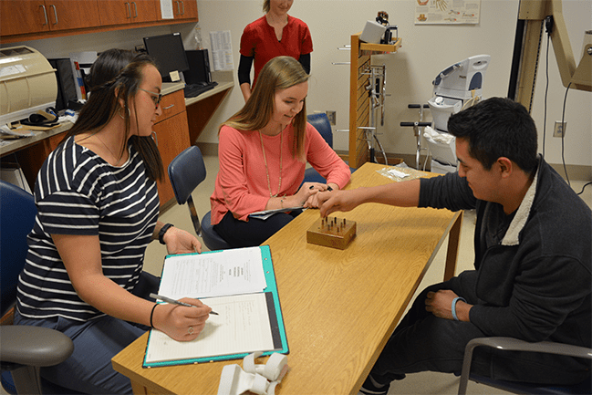 Occupational therapy student helping a patient while a supervisor looks on.