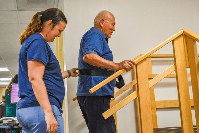 A physical therapist helps an older male patient climb stairs