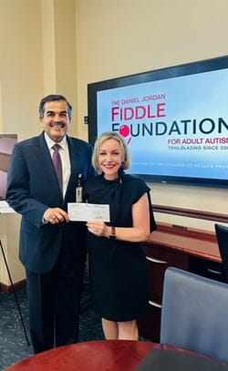 Dean Zoher Kapasi and Linda Walder, founder and CEO of The Daniel Jordan Fiddle Foundation, hold a check while standing in front of a screen with the DJFF logo.