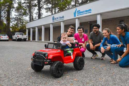 students pose with adaptive car and child