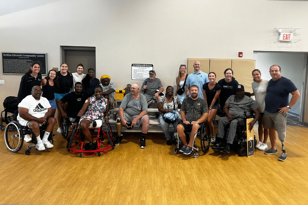 MUSC OTD students stand in a group with participant from their inaugural wheelchair pickleball tournamant inside a gym.