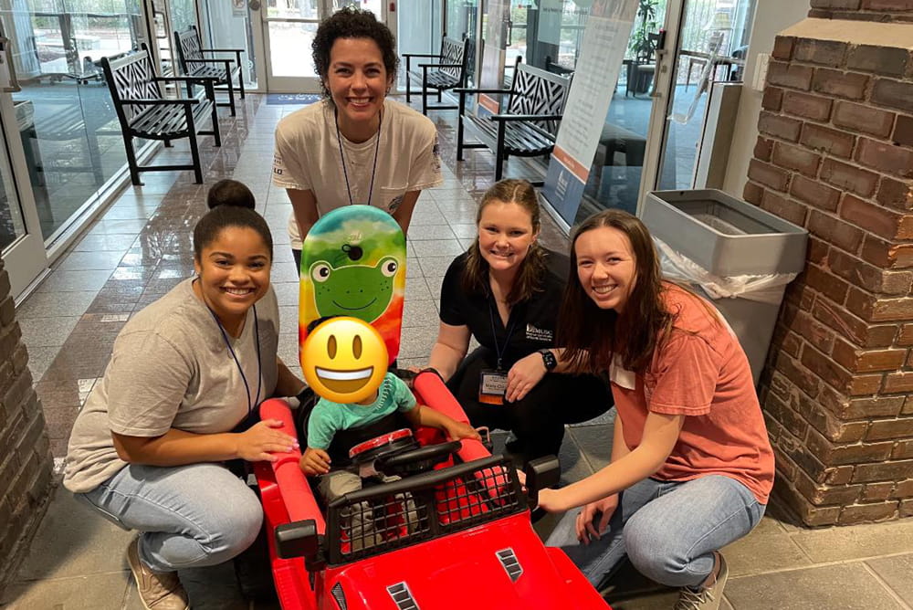 students pose with a child in an adaptive vehicle