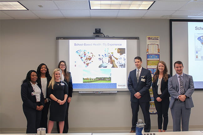 Master of Health Administration students standing in front of a classroom.