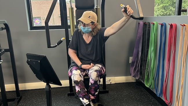 Woman wearing baseball cap and face mask does arm exercise in the NExT Center