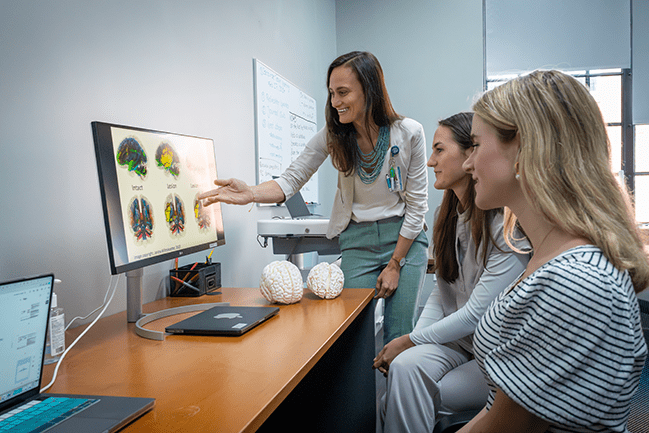 woman teaching two students in front of monitor