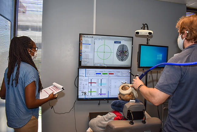 Study participant recieves brain stimulation for rehab from 2 research therapists